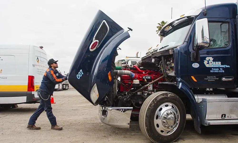 Mechanic lifting the hood of a dark blue Peterbilt truck