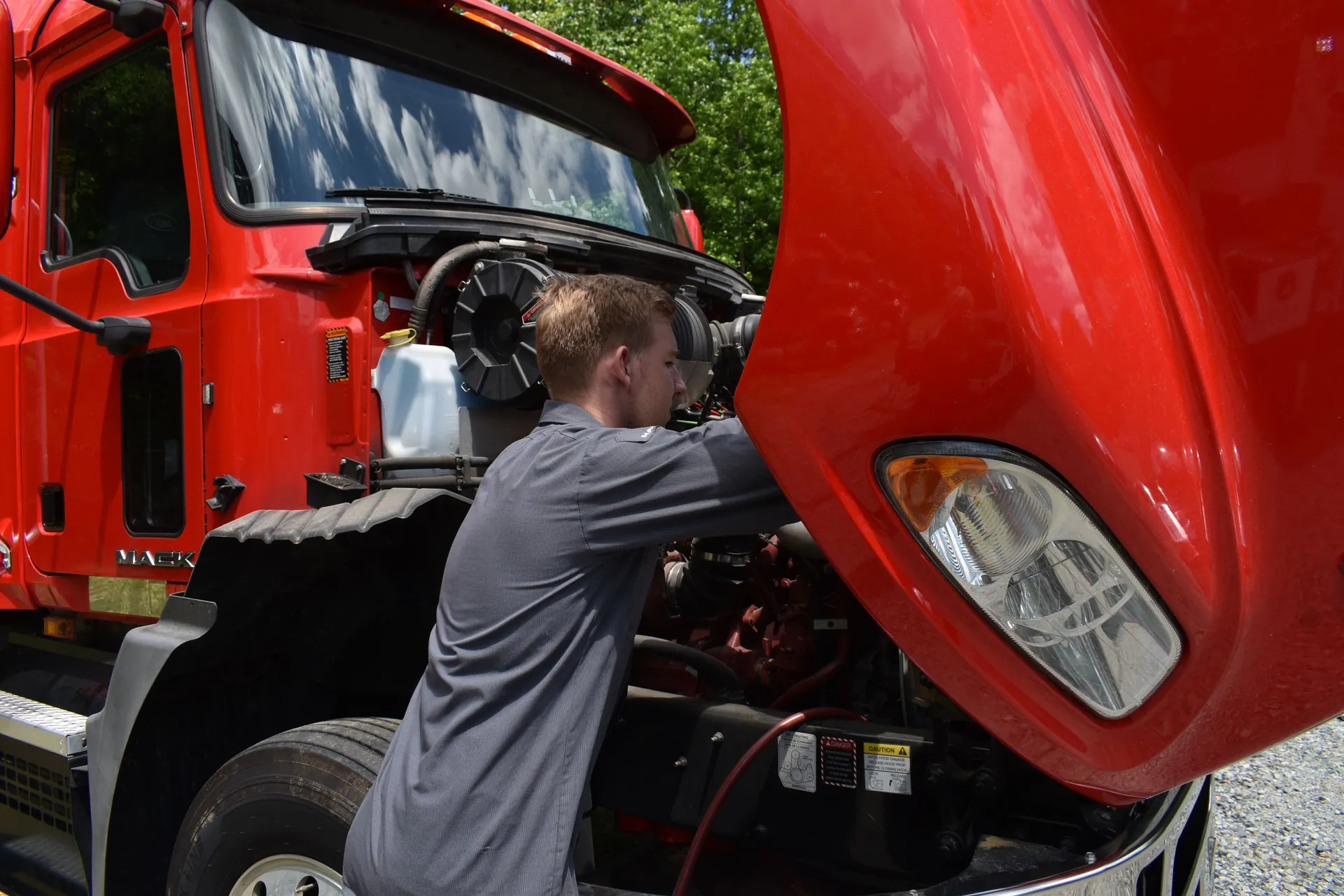 Technician servicing the engine of a red Mack truck